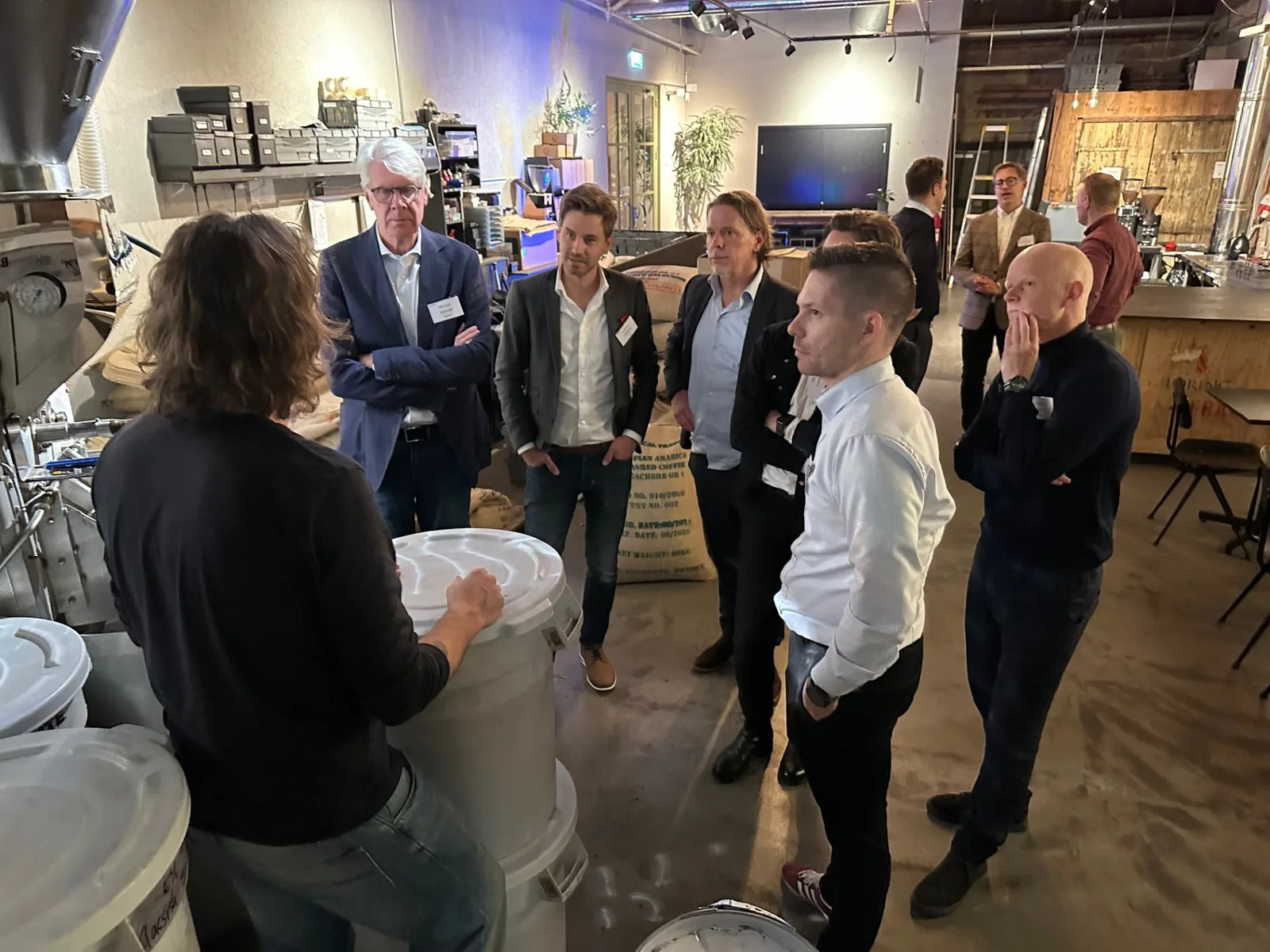 Gäster på Coact & friends i da Matteos rosteri på Magasinsgatan i Göteborg, samlade runt en visning bland kaffesäckar och rostmaskin.